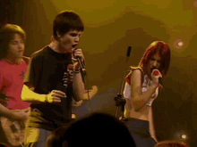 a man singing into a microphone while playing a guitar and a woman singing in front of a crowd .