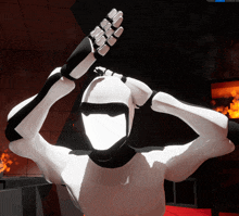 a white robot with black gloves is standing in a dark room with a fire in the background