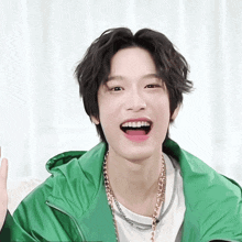 a young man with braces on his teeth is wearing a green jacket and a necklace
