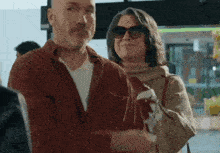 a man and woman are standing next to each other and the woman is wearing sunglasses
