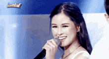 a woman is smiling while singing into a microphone on stage .