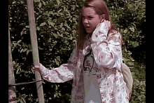 a young girl is standing in front of a tree holding a stick and wearing a floral shirt .