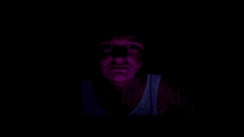 a person 's face is visible in the dark and they are wearing a white tank top