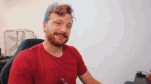 a man with a beard is sitting in a chair in front of a fan .