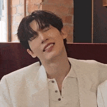 a young man wearing a white jacket is making a funny face with his eyes closed .