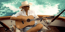 a man in a cowboy hat is sitting on a boat playing a guitar