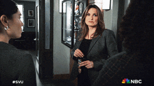 a woman standing in a hallway with a nbc logo on the bottom of the screen
