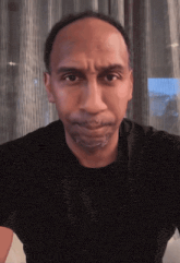 a man in a black shirt looks at the camera with a serious look on his face