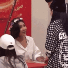 a woman wearing a flower crown is talking to a man in a baseball cap .