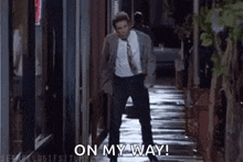 a man in a suit and tie is walking down a sidewalk and says `` on my way '' .
