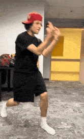a man wearing a red hat and black shorts is dancing in a hallway