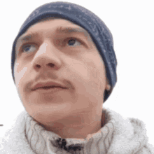 a man wearing a blue beanie and a white sweater looks up at the sky .
