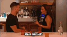 a man and a woman are sitting at a table with a fan behind them and the woman says klein meisje