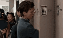 a young man is standing in front of a locker in a hallway .