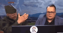 two men sitting in front of a computer with a sticker that says jk