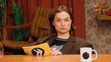 a woman sitting at a table holding a piece of paper that says ' i 'm sorry ' on it