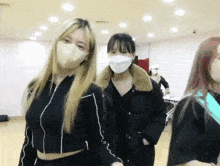 a group of women wearing masks are standing in a room .
