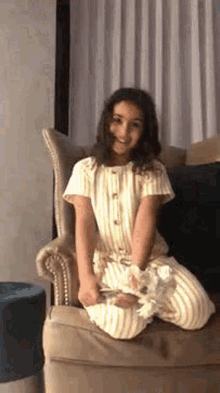 a little girl is sitting in a chair with her legs crossed and holding a pillow .