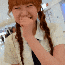 a girl with pigtails is covering her mouth with her hand and smiling