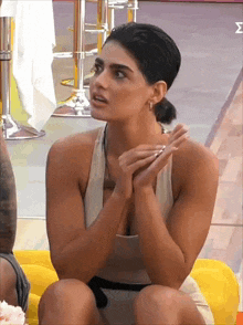 a woman in a white tank top is sitting on a yellow couch with her hands folded