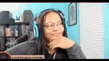 a woman wearing headphones and glasses is sitting in front of a screen that says later jacquese playing .