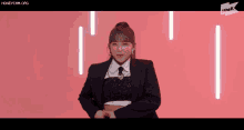 a girl in a suit and tie is dancing on a pink background .
