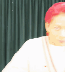 a woman with red hair and a white shirt is standing in front of a green curtain