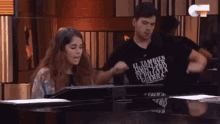 a man and a woman are dancing in front of a piano . the man is wearing a shirt that says el tambien