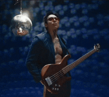 a man with a tattoo on his chest is holding a guitar in front of a disco ball