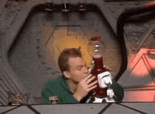 a man in a green shirt is smoking a bong with a clock in the background