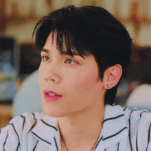 a close up of a young man 's face with a striped shirt and earrings