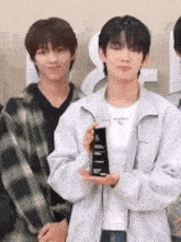a young man is holding a trophy in his hand while standing next to another young man in a plaid shirt .