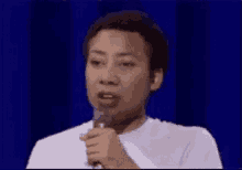 a woman is holding a microphone in front of a blue curtain and saying good .