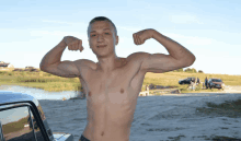 a shirtless man flexes his muscles in front of a lake