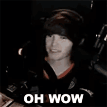 a man wearing headphones is sitting in front of a microphone with the words oh wow written on the screen .