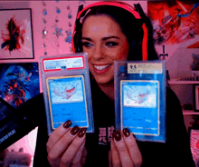 a woman wearing headphones is holding two pokemon cards one of which has a 9.5 on it