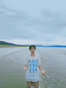 a man wearing a shirt that says rustys sco is standing in the water