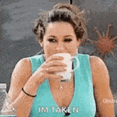 a woman in a blue tank top is drinking from a white cup .