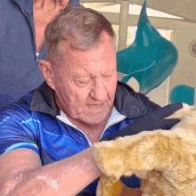 an older man in a blue shirt is petting a stuffed animal