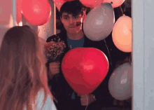 a man is holding a heart shaped balloon in front of a woman holding a bouquet of flowers .