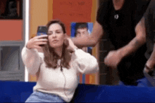 a woman is sitting on a couch taking a selfie with a cell phone .