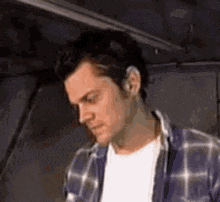 a man in a plaid shirt is standing in a dark room .
