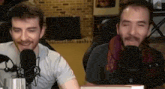 two men are sitting in front of microphones in a room .