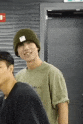 a man wearing a beanie and a green shirt is standing next to another man in a room .