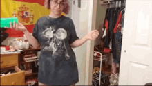 a woman wearing a t-shirt with a cat on it is standing in a closet holding a green box .