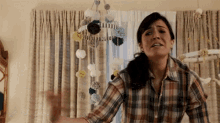 a woman in a plaid shirt is standing in a room with a baby mobile hanging from the ceiling .