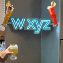 a neon sign that says wxyz on it with two drinks in front of it