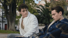 two young men are sitting on a bench looking at something