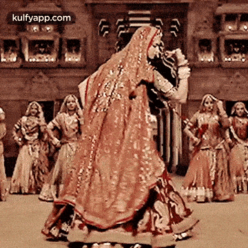 a bride and groom are dancing in front of a group of women in traditional indian dresses .