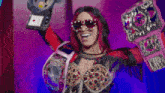 a woman wearing sunglasses is holding up a wrestling belt .